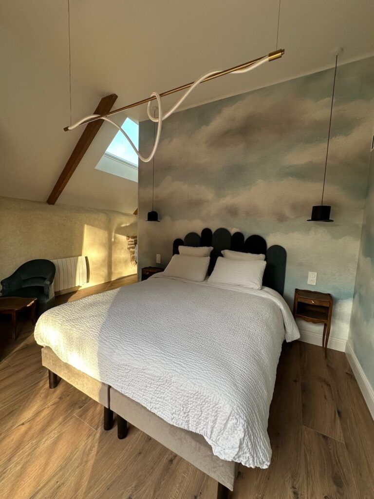 Lit queen size avec papier peint nuages et liseuse chapeau melon – Chambre surréaliste L'Empire des Songes, Les Reflets Roz